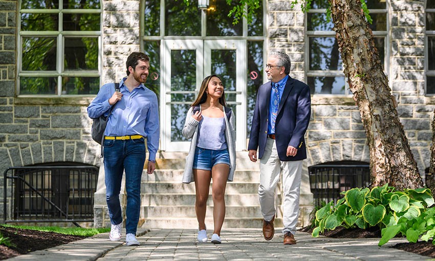 Faculty member walking with two ר students outside Tolentine Hall.