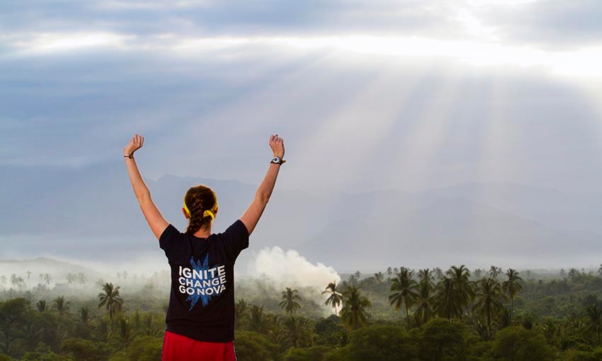 Female student in ר shirt raises arms above head as she looks over landscape of Peru.